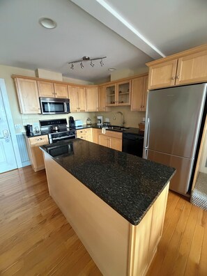 A modern kitchen with wooden cabinets, a granite countertop, stainless steel appliances, and a central island. - Trade Winds on the Bay (Rockland)