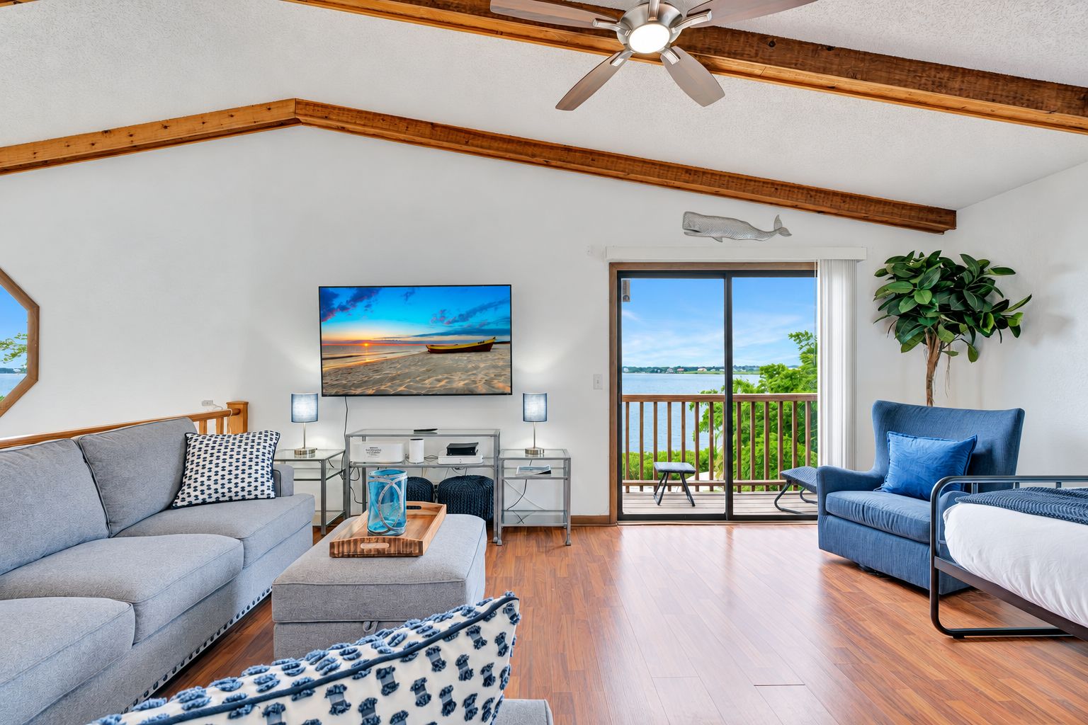 Een ruime woonkamer met een bank, een salontafel, een televisie en een balkon met uitzicht op het water.