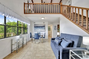 A spacious living area with a dining table, blue chairs, a blue sofa, and a staircase with wooden railings.
