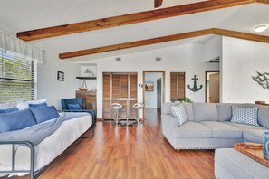A spacious living room with a wooden floor, a grey sofa, a blue sofa, and a small table with two stools.