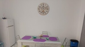 A dining area with a marble floor, a white table, four chairs with green cushions, and a wall clock. - Apartment Giorgia 1 (Campofelice di Roccella)