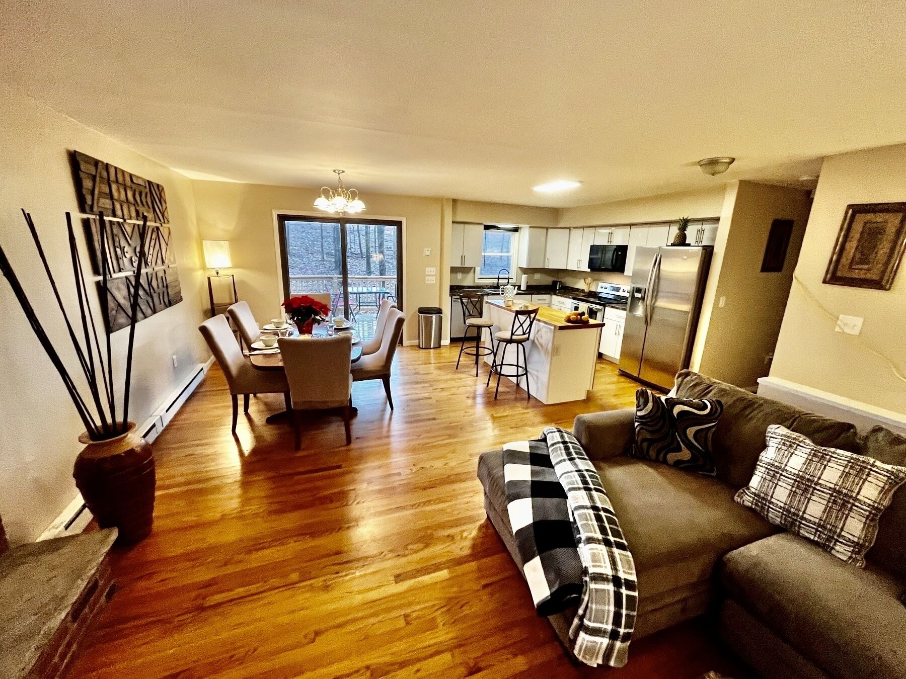 A modern living room with a sofa, a dining table with chairs, and a kitchen area with a refrigerator and microwave.