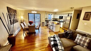 A modern living room with a sofa, a dining table with chairs, and a kitchen area with a refrigerator and microwave.