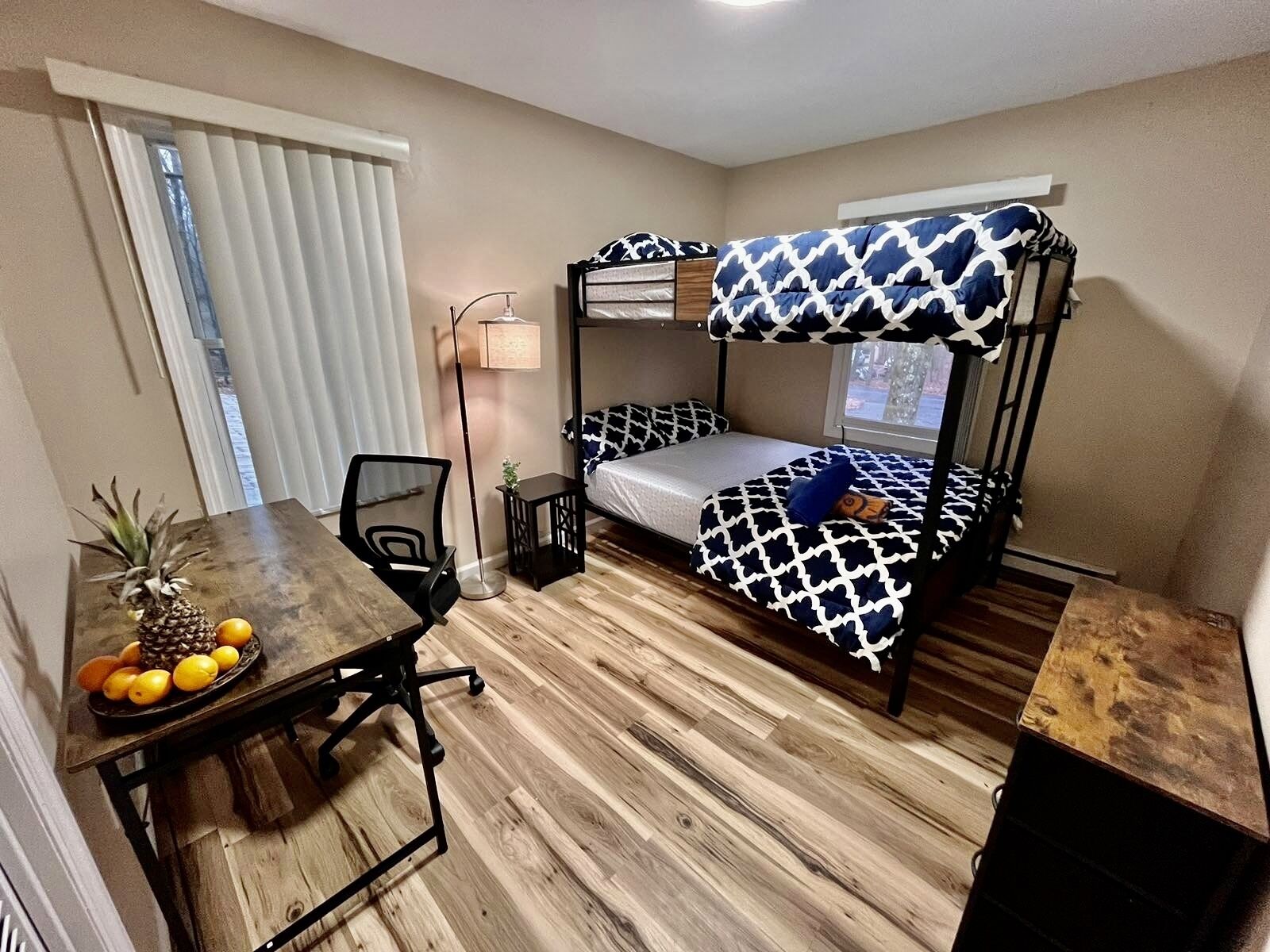 A compact room with a bunk bed, a desk with a pineapple and oranges, and a floor lamp.