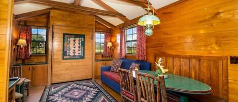 Un interior de cabaña acogedor con una mesa de comedor de madera, un sofá azul y una alfombra estampada.