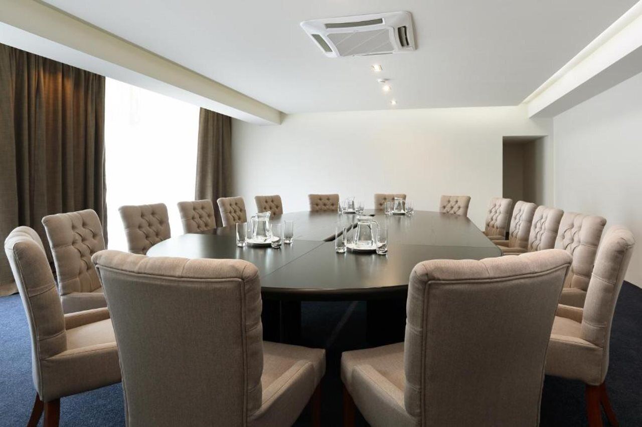 A conference room with a round table, beige upholstered chairs, and a white ceiling air conditioning unit.