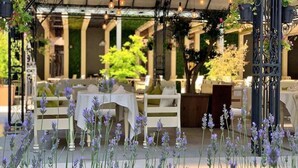 Un espacio de comedor al aire libre con mesas y sillas, una zona de estar cubierta y plantas colgantes.