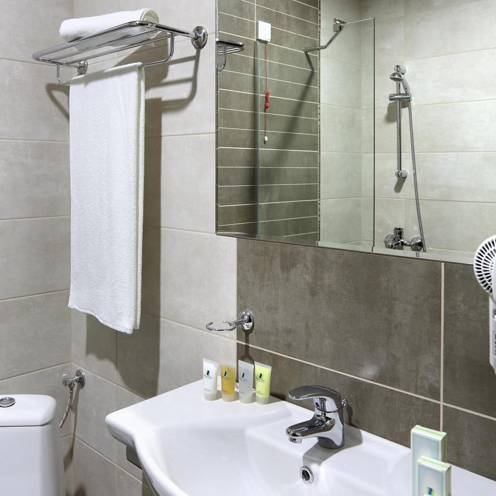 Un baño con un lavabo blanco, un espejo, un perchero para toallas y una ducha.