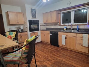 A kitchen with wooden cabinets, a dishwasher, a stove, and a window above the sink. - EV Charging BirdHouse (Emporia)