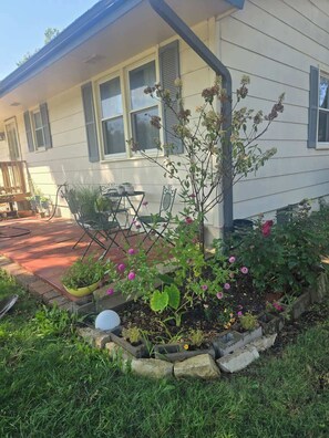 A house with a front porch, a small garden with flowers, and a metal chair.
