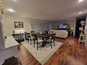 A living room with a dining table, chairs, a sofa, a TV, and a kitchen area.