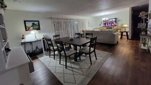 A dining area with a table and chairs, a sofa, a television, and a staircase.