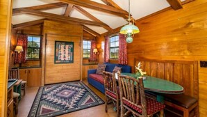 A cozy cabin interior with a wooden dining table, a blue sofa, and a patterned rug.