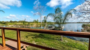A wooden deck overlooking a lake with a bridge, surrounded by trees and grassy areas.