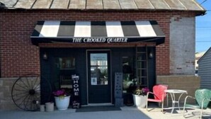 Een gebouw met een zwart-wit gestreept luifel en het bord 'THE CROOKED QUARTER'.