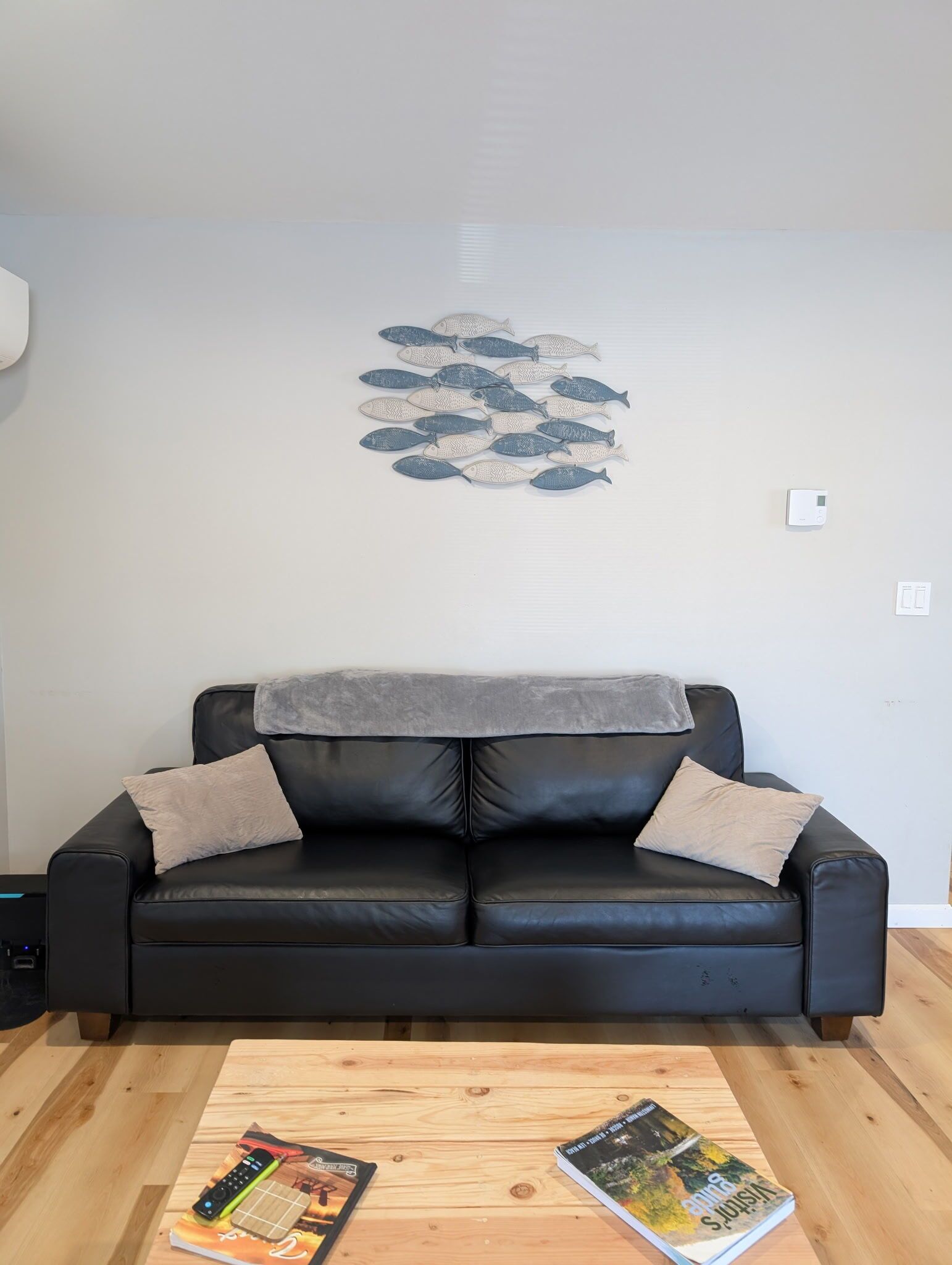 A black leather sofa with a blanket, two pillows, and a wooden coffee table with books and a remote control.