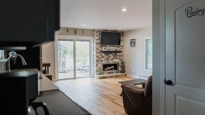A modern living room with a stone fireplace, a flat-screen TV, and a sliding glass door leading to an outdoor area. - Beaver Lake Escape
 (Rock Hill)