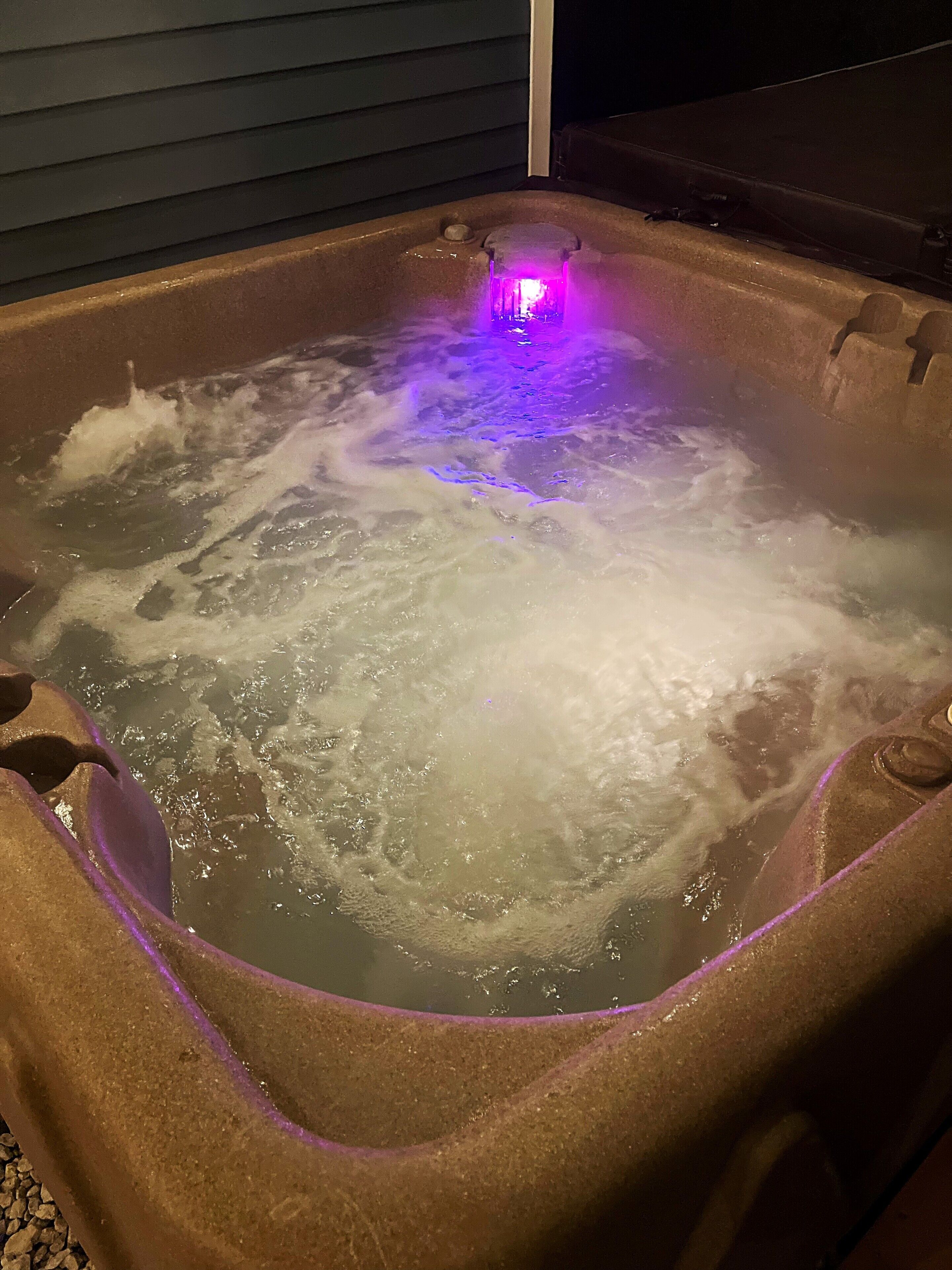 Un bain à remous avec un éclairage violet, entouré d’une structure qui ressemble à de la pierre.