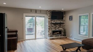 A spacious living room with a fireplace, a flat-screen TV mounted above it, and a sliding glass door leading to an outdoor area. - Beaver Lake Escape
 (Rock Hill)