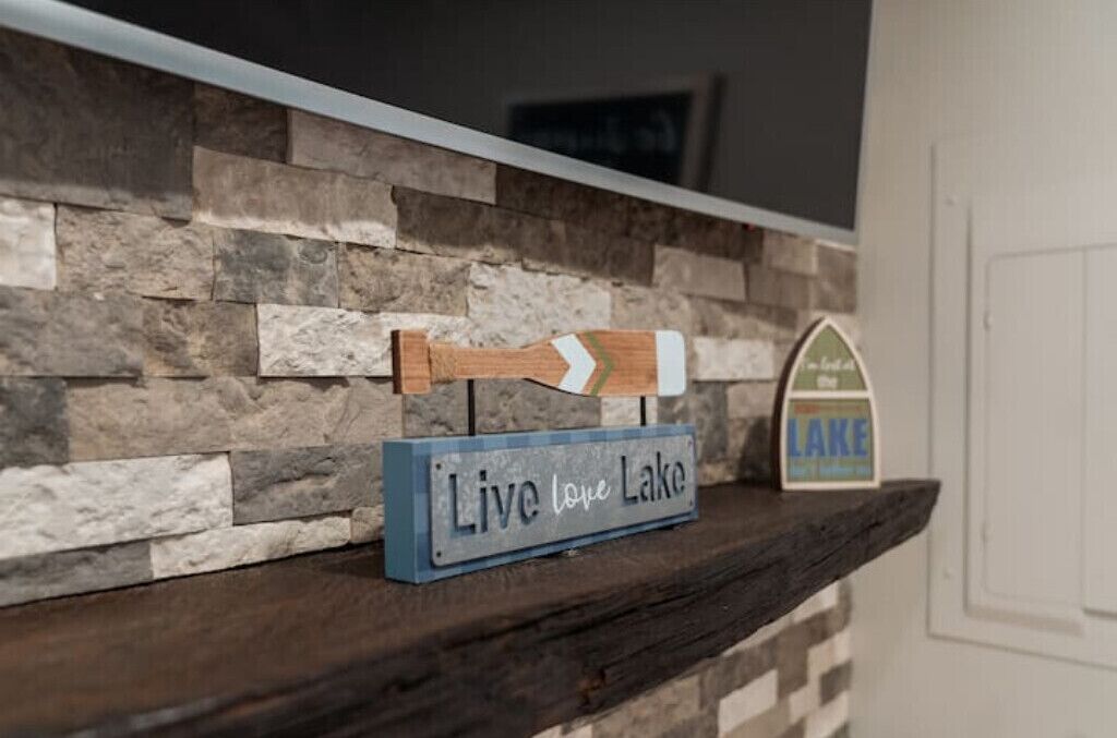 Un muro de piedra rústica con un letrero de madera que dice “Live love Lake” y una señal con una flecha direccional.