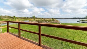 Una terraza de madera con barandilla que da a un área verde y una masa de agua.