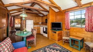 Una cabaña acogedora con interior de madera, una zona de comedor con mesa y sillas, un televisor y un ventanal con cortinas.