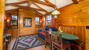 Ein gemütliches Blockhaus-Interieur mit einem Holzesstisch, einem blauen Sofa und einem gemusterten Teppich.