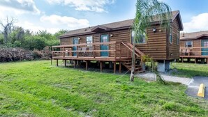 Una cabaña de madera con terraza, rodeada de césped y árboles.