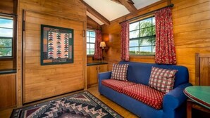 Interior acogedor de una cabaña con paredes de madera, un sofá azul, cortinas estampadas y una alfombra.