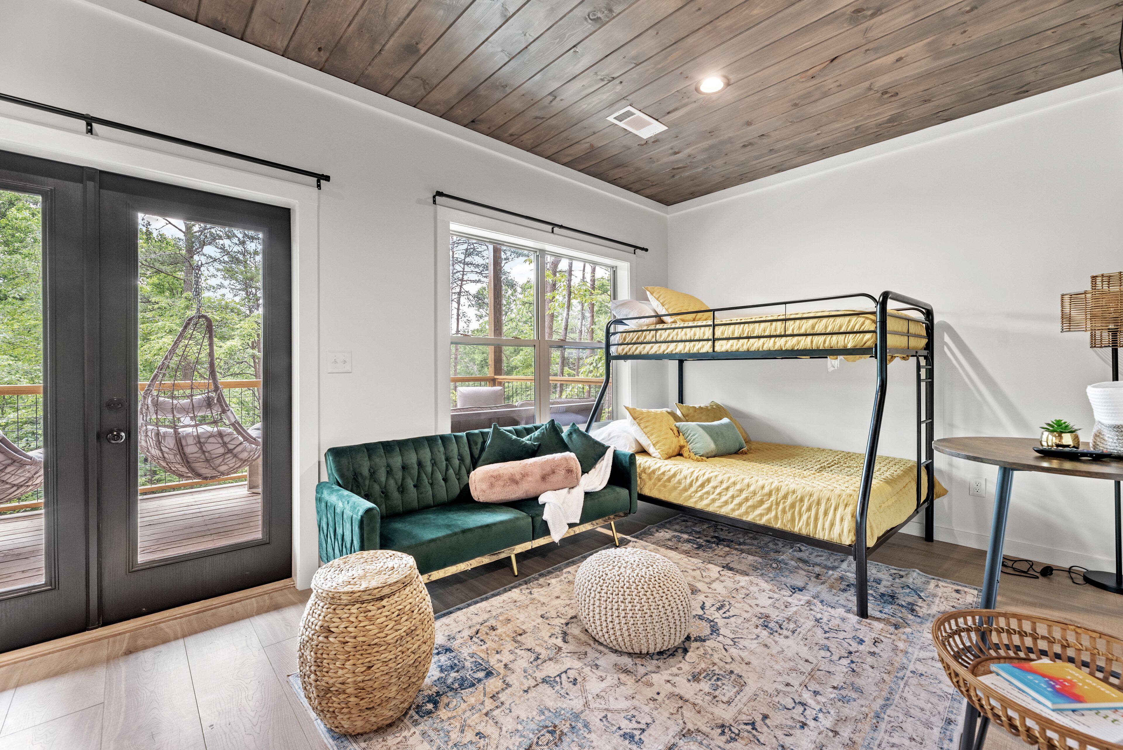 A room with a bunk bed, a green sofa, a woven ottoman, and a round table with a book.