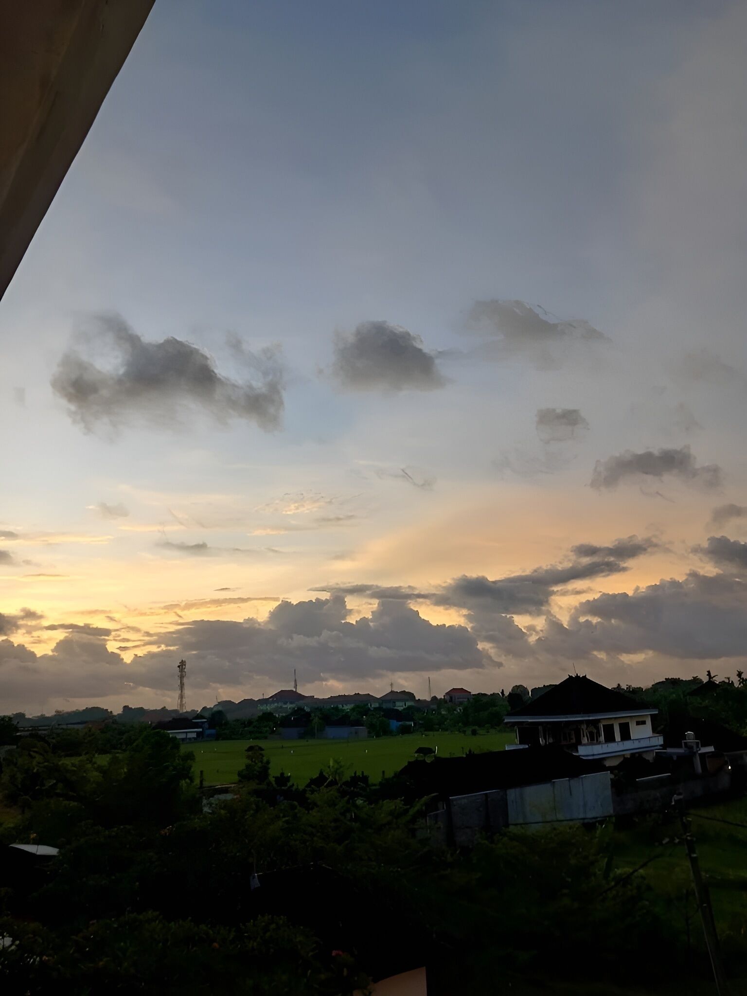 Un paysage rural avec des maisons, un champ et un ciel nuageux.