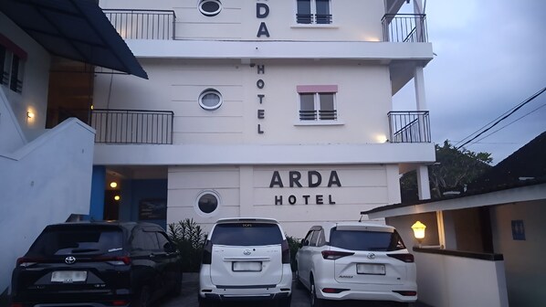 A multi-story building with the sign "ARDA HOTEL" prominently displayed. There are two white cars parked in front, and the building has balconies on the upper floors. - Hotel Arda Bali (Negara)