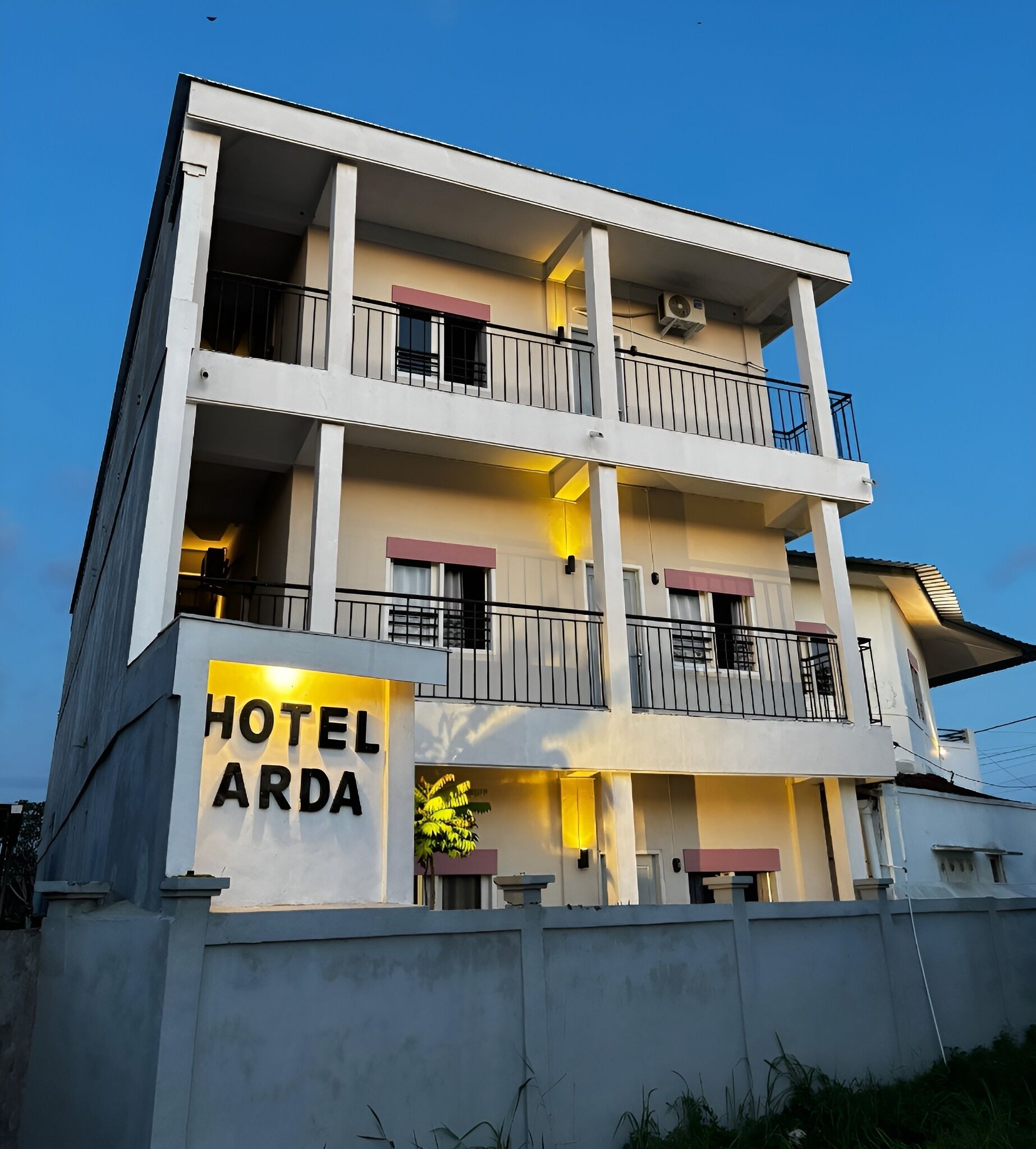 Ein mehrstöckiges Hotel mit Balkonen, einem Schild mit der Aufschrift "HOTEL ARDA" und blauem Himmel im Hintergrund.