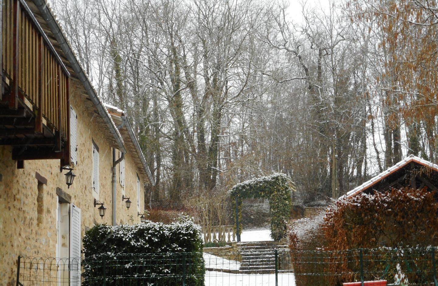 Un bâtiment à la façade de style traditionnel, un jardin recouvert de neige et une clôture en bois.