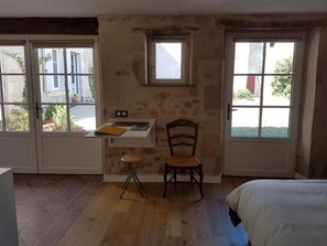 A room with a bed, a desk with a chair, a small table, and two windows.