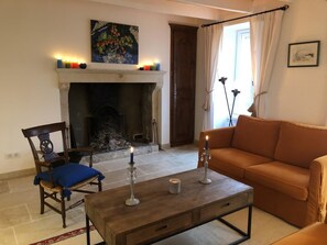 Uma sala de estar com lareira, um sofá, uma poltrona e uma mesa com velas.