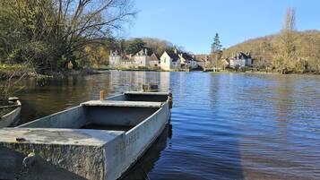 A calm river with boats docked, a clear sky, and houses in the background.