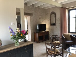 A room with a TV on a wooden cabinet, a mirror on the wall, and a vase with flowers on a dresser.