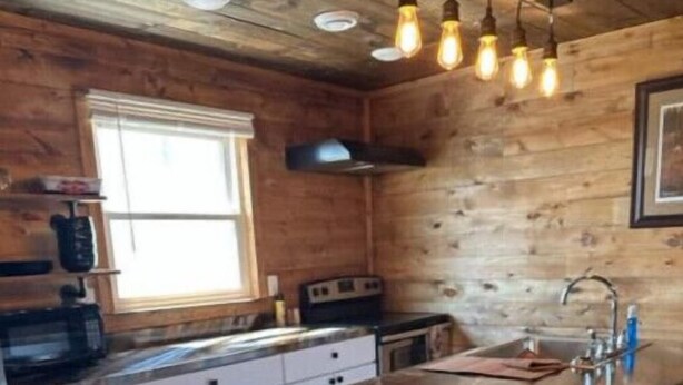 Une cuisine dotée d’un grand îlot central, de murs en bois et de luminaires suspendus.