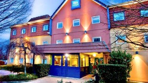 Un hotel de dos pisos con fachada roja y color beige, un llamativo letrero 'ibis budget' y una entrada bien iluminada.