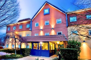 Un hotel de dos pisos con fachada roja y color beige, un llamativo letrero 'ibis budget' y una entrada bien iluminada.