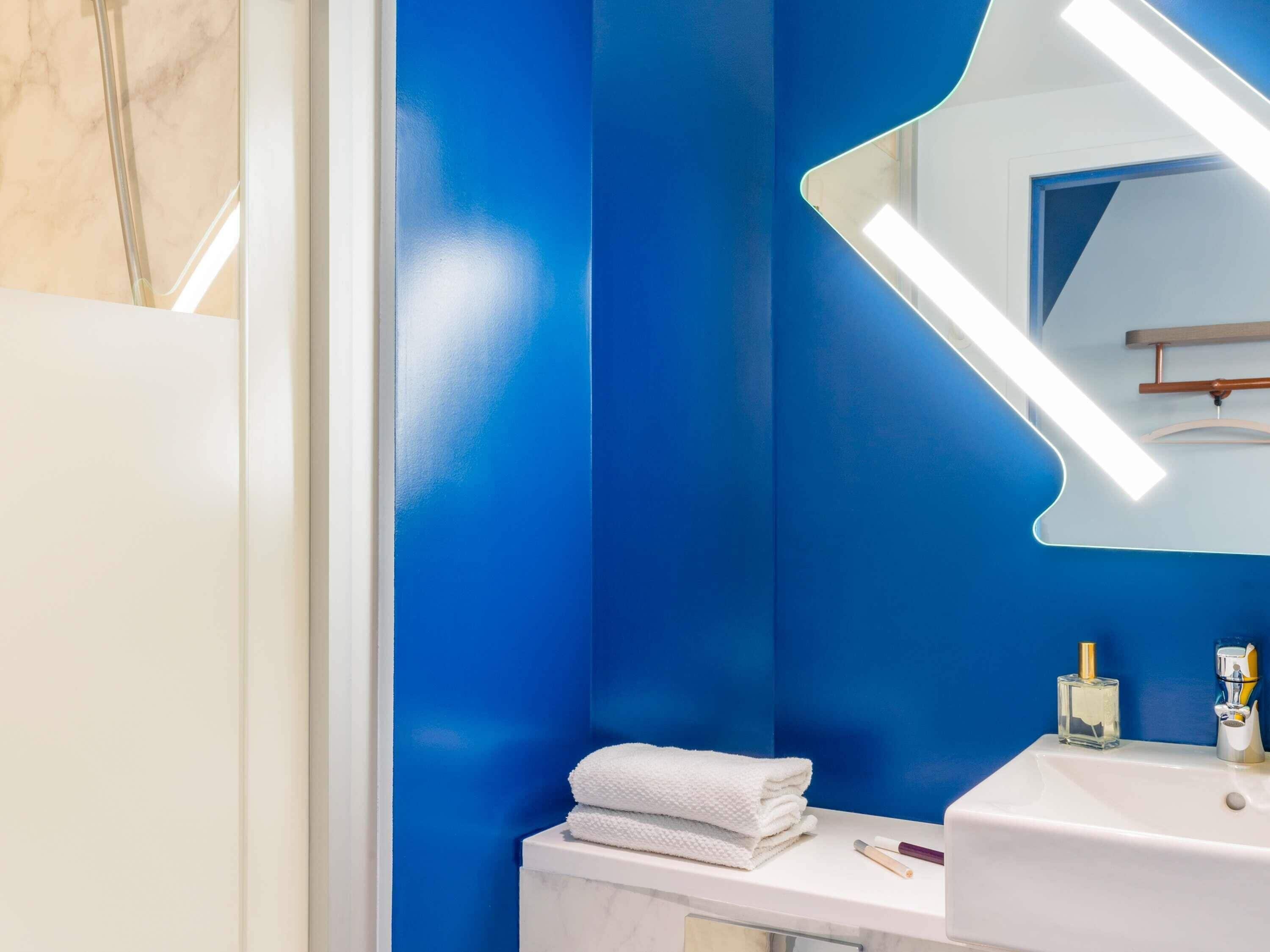 Un bagno con un lavandino bianco, uno specchio e una parete azzurra.