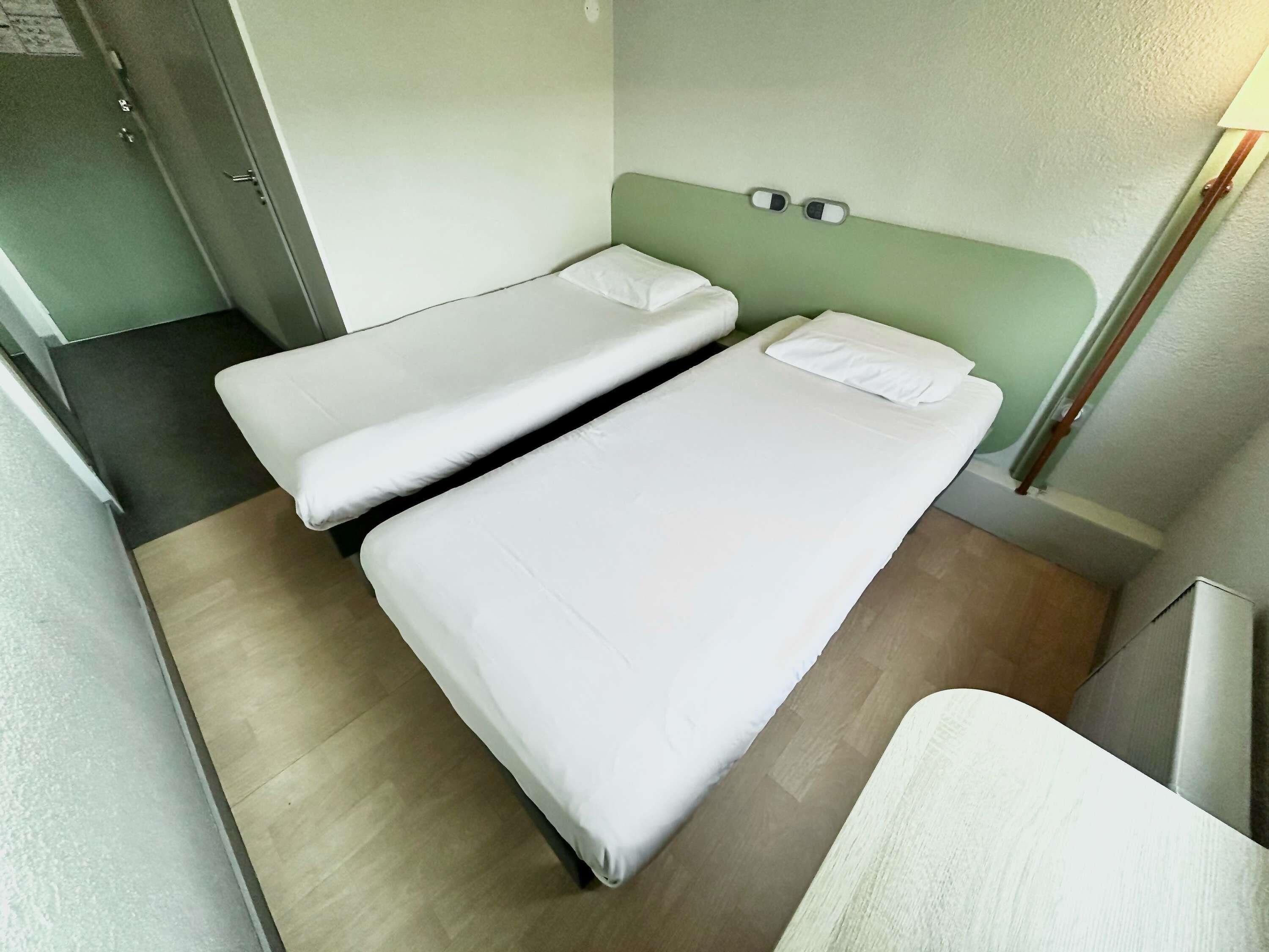 Une petite pièce, de taille modeste, comprenant deux lits simples, une porte et un petit coin salon.