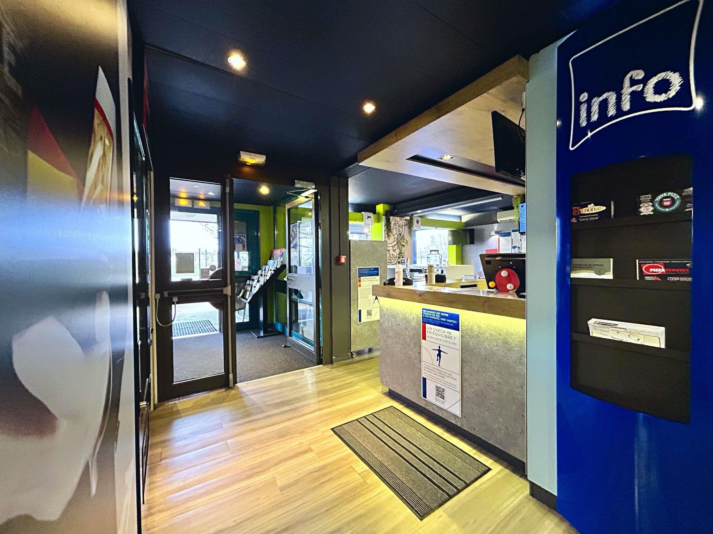 Un área de recepción con un mostrador de información azul, una escalera y una mesa de registro.