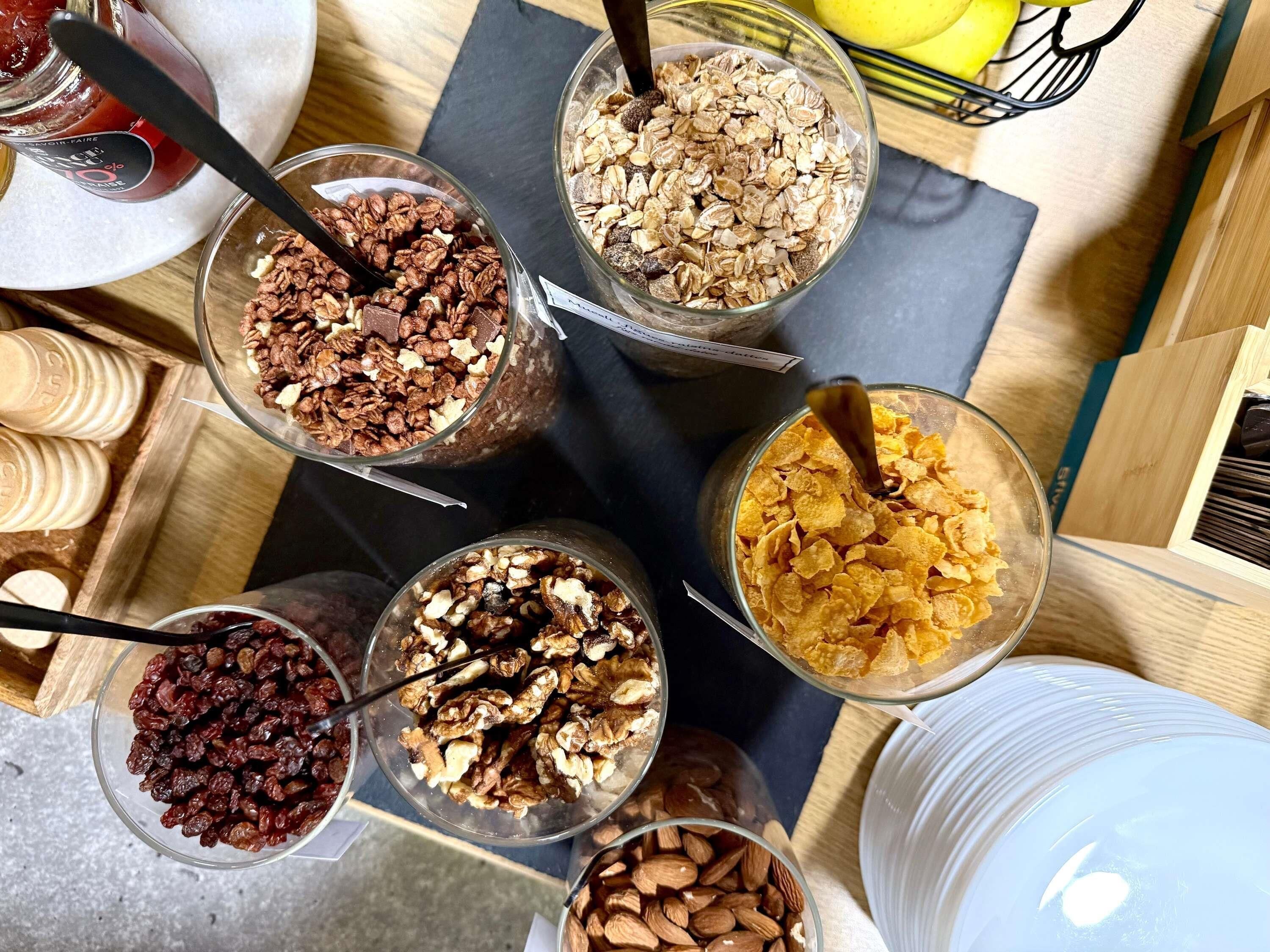 A variety of food items in bowls, including granola, nuts, and dried fruits, arranged on a wooden table.
