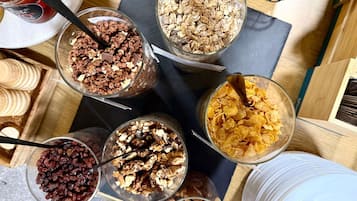 A variety of food items in bowls, including granola, nuts, and dried fruits, arranged on a wooden table.