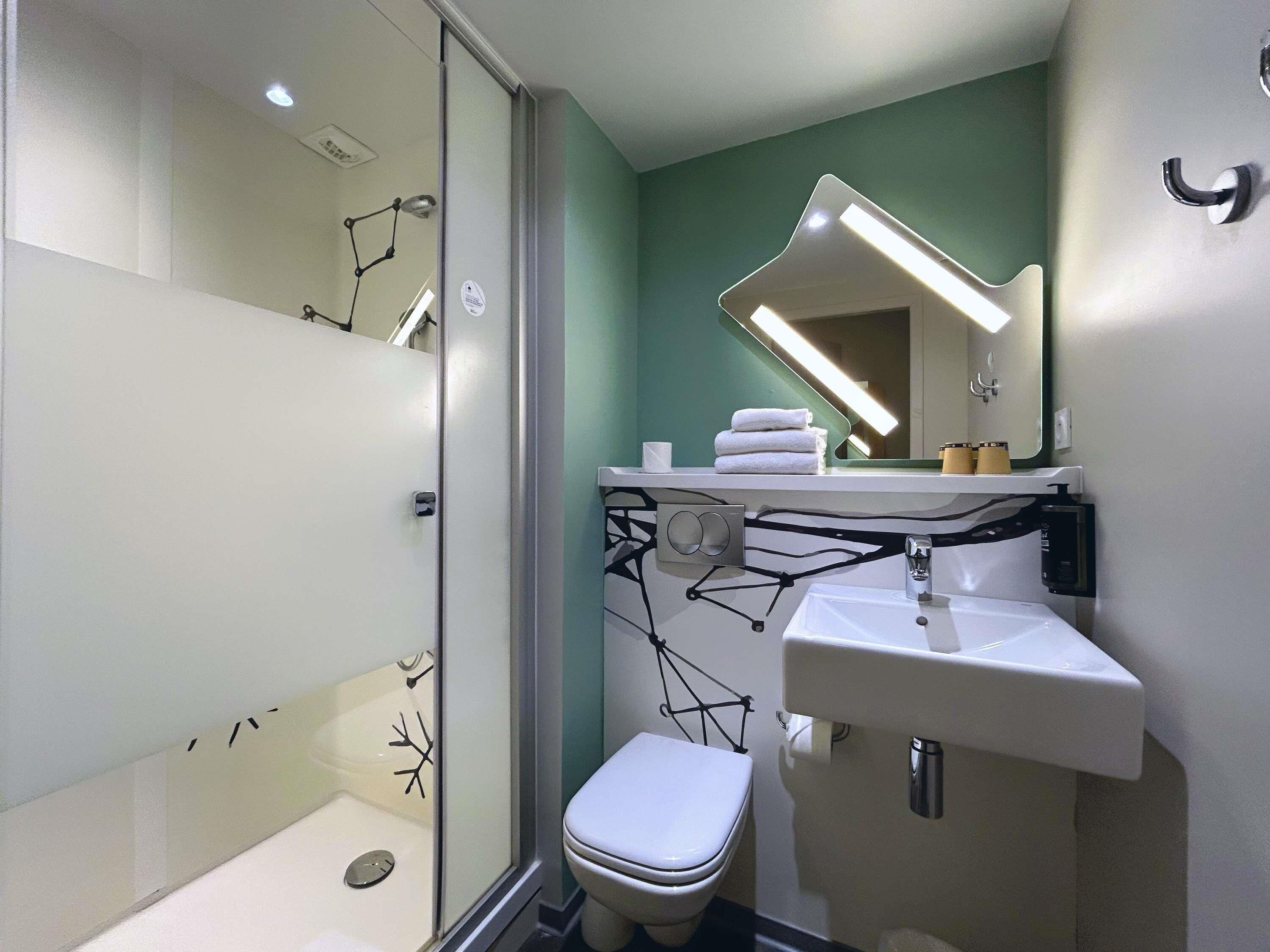 Un baño con cabina de ducha de vidrio, inodoro blanco, lavamanos con espejo y toallero.