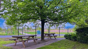 Una mesa de picnic bajo un árbol en un parque, con un parque infantil al fondo.