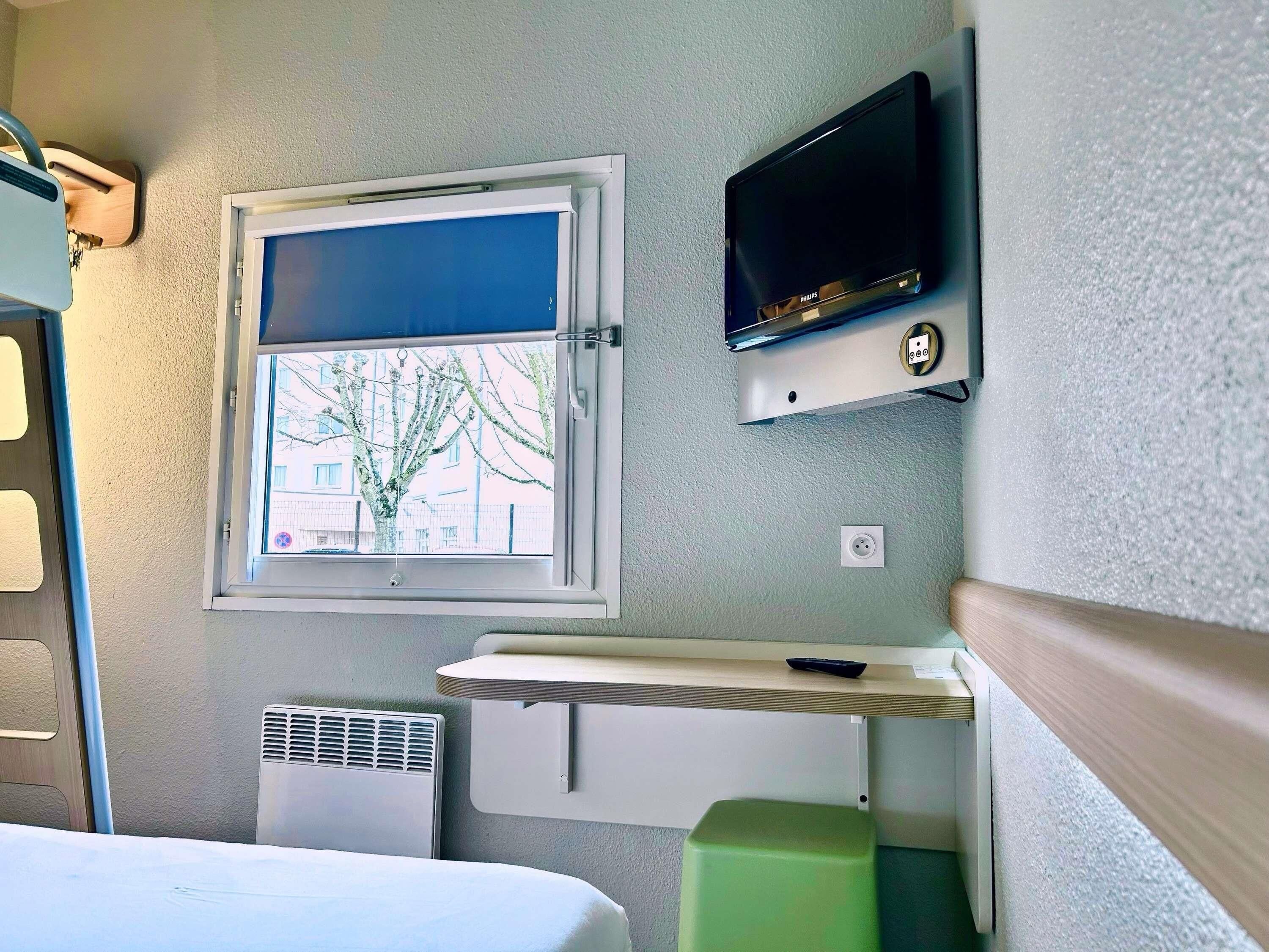 A compact room with a window, a wall-mounted TV, a desk, and a bed.