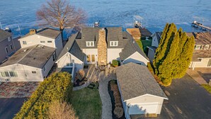 A residential area with houses, a driveway, and a body of water in the background. - Beautifully updated home on the bay and golf course with dock and raised deck! (Sodus Point)